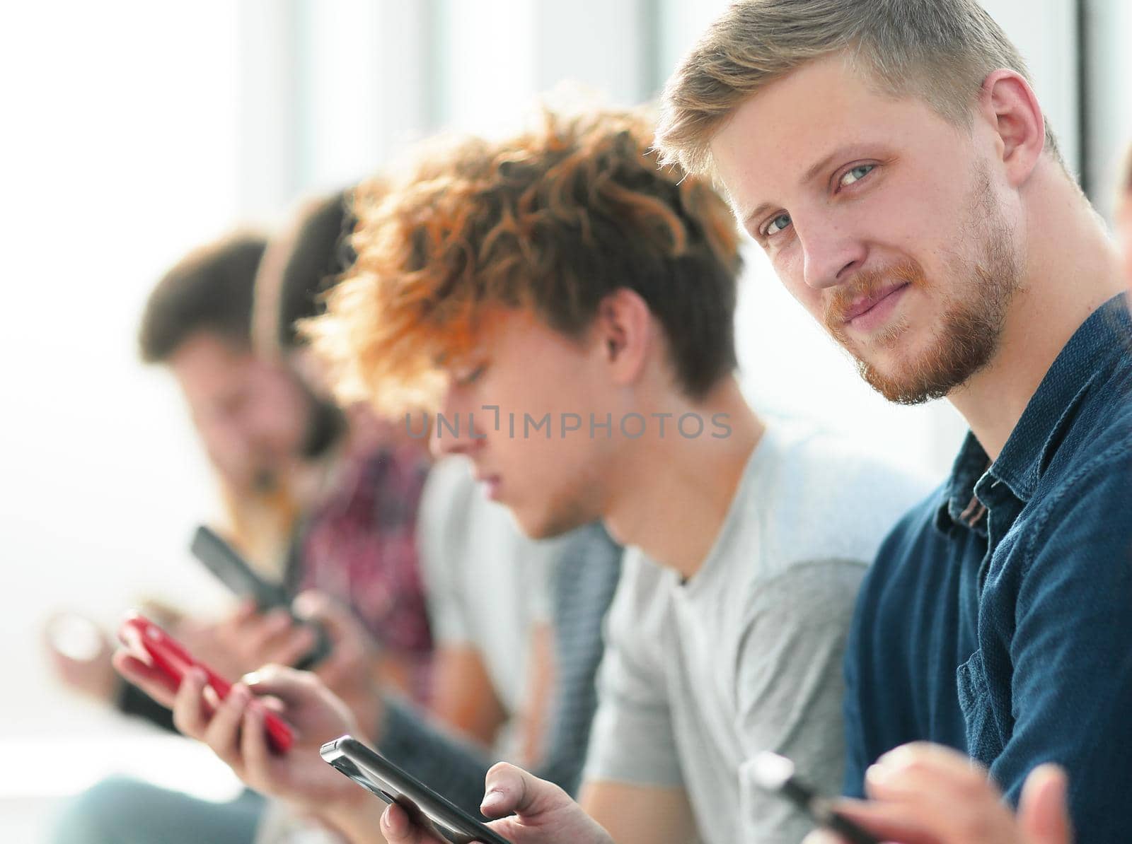 group of young people with smartphones sitting in one row by asdf
