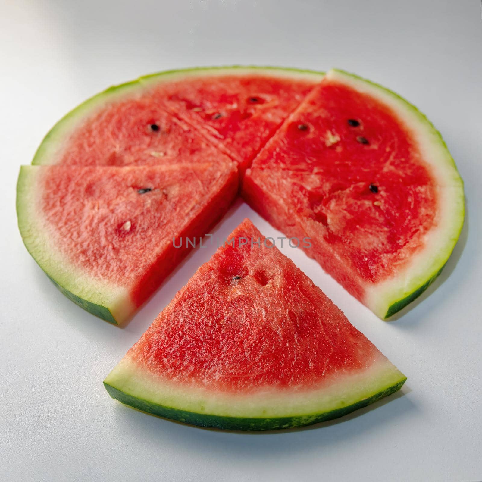 Slices of fresh red delicious watermelon are laid out in a circle on a colored background.