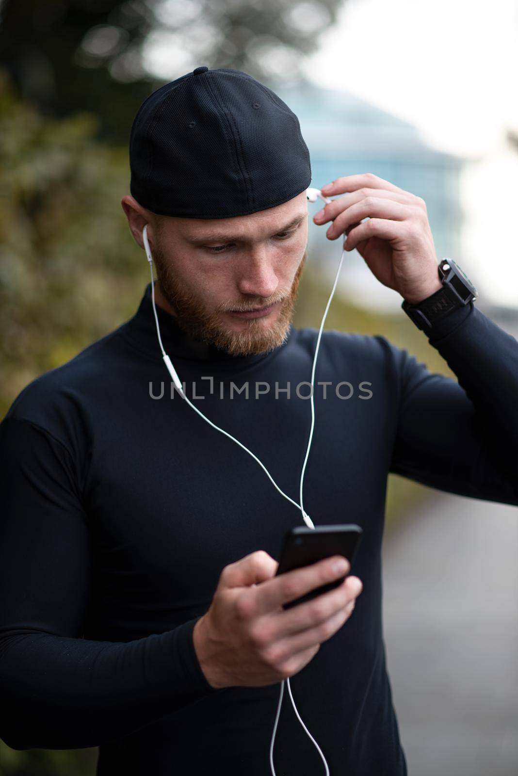 Close-up shot of young white man with beard putting headphone in his ear by Nickstock