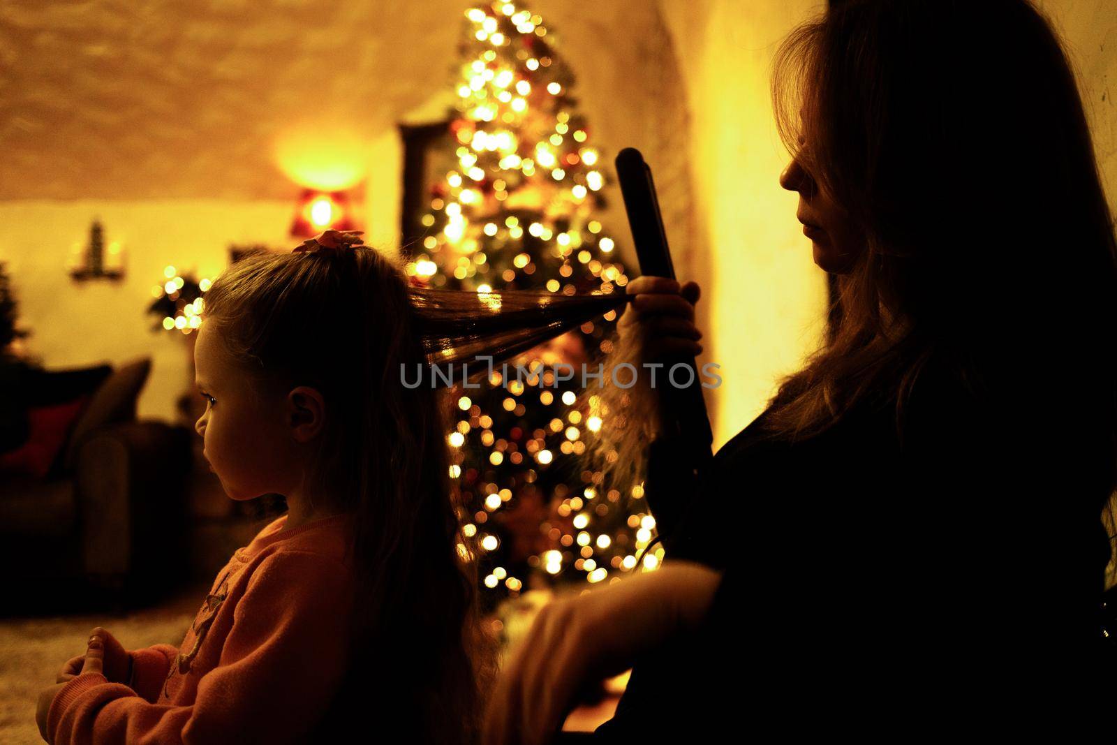 Mom combing her daughter for a festive dinner in the room with a christmas tree. Selective soft focus, film grain effect