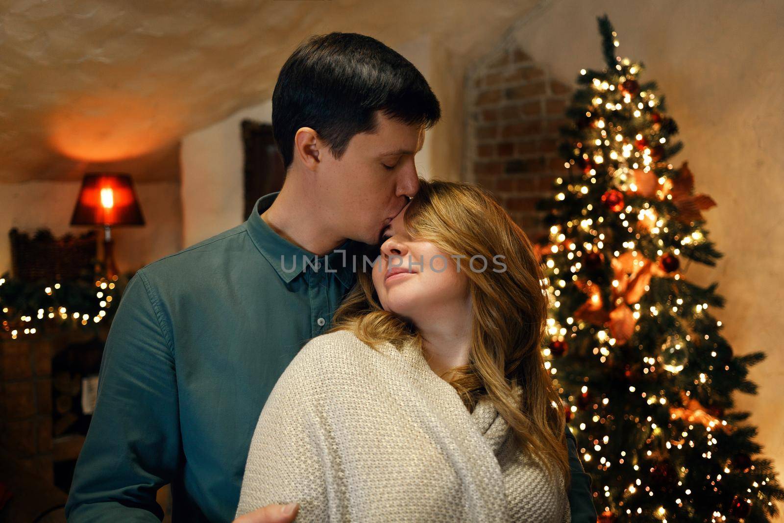 Beautiful middle aged caucasian couple posing in new year interior with a christmas tree and garlands. Selective soft focus, film grain effect