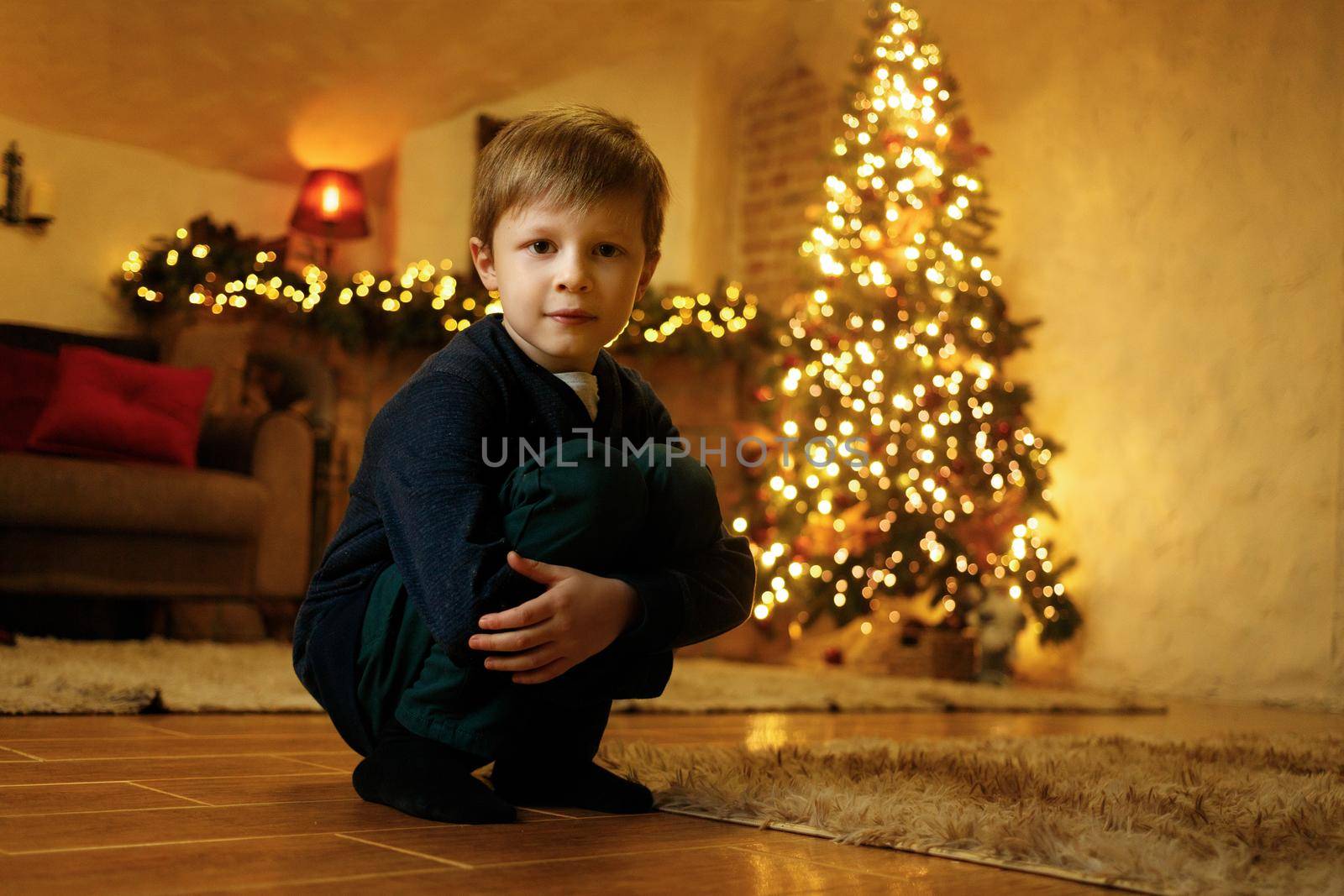 A boy sits on the floor in a festive room on the eve of the new year by Rom4ek