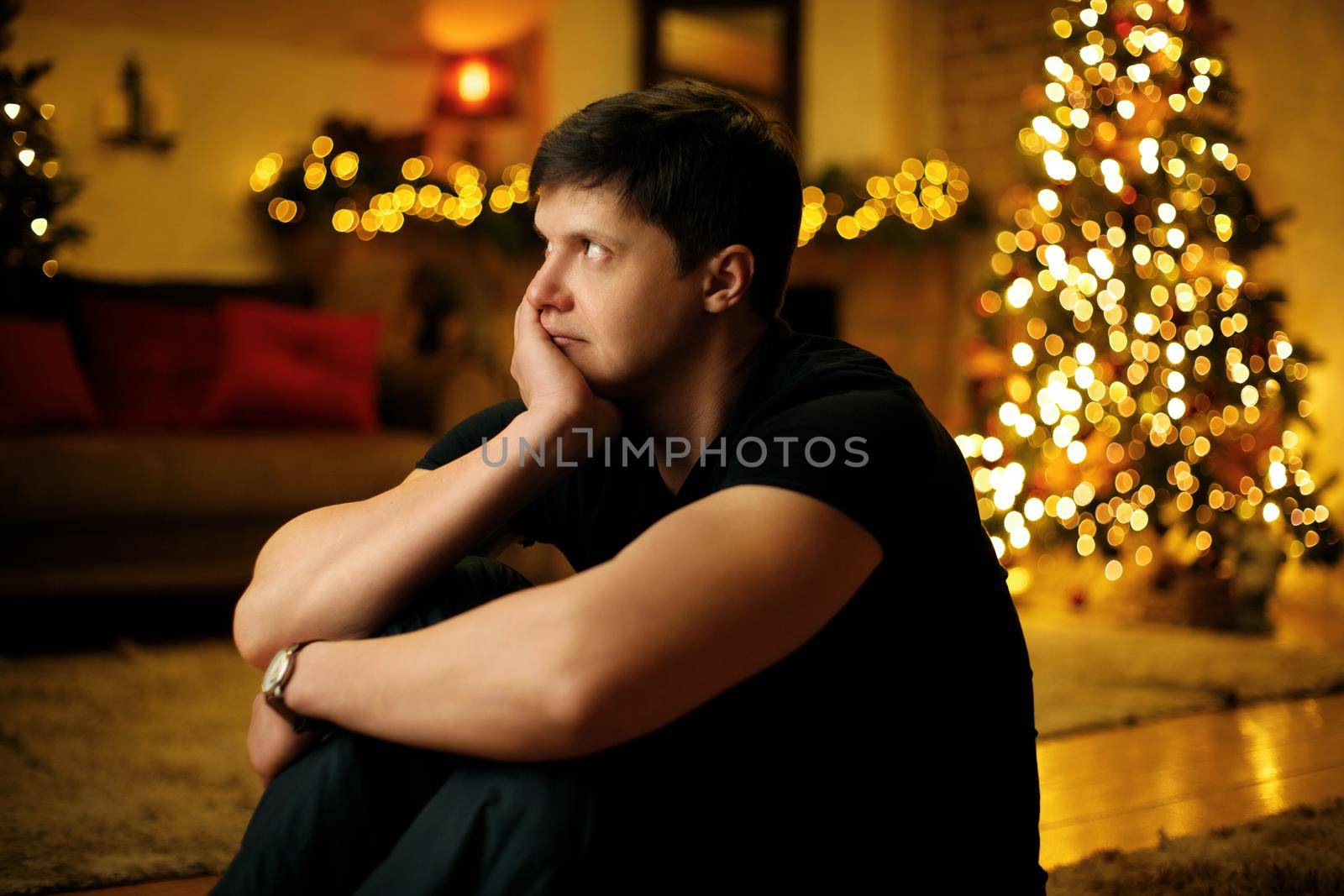 Lonely young man bored in a room decorated with a festive christmas tree and garlands on new years eve. Selective soft focus, film grain effect