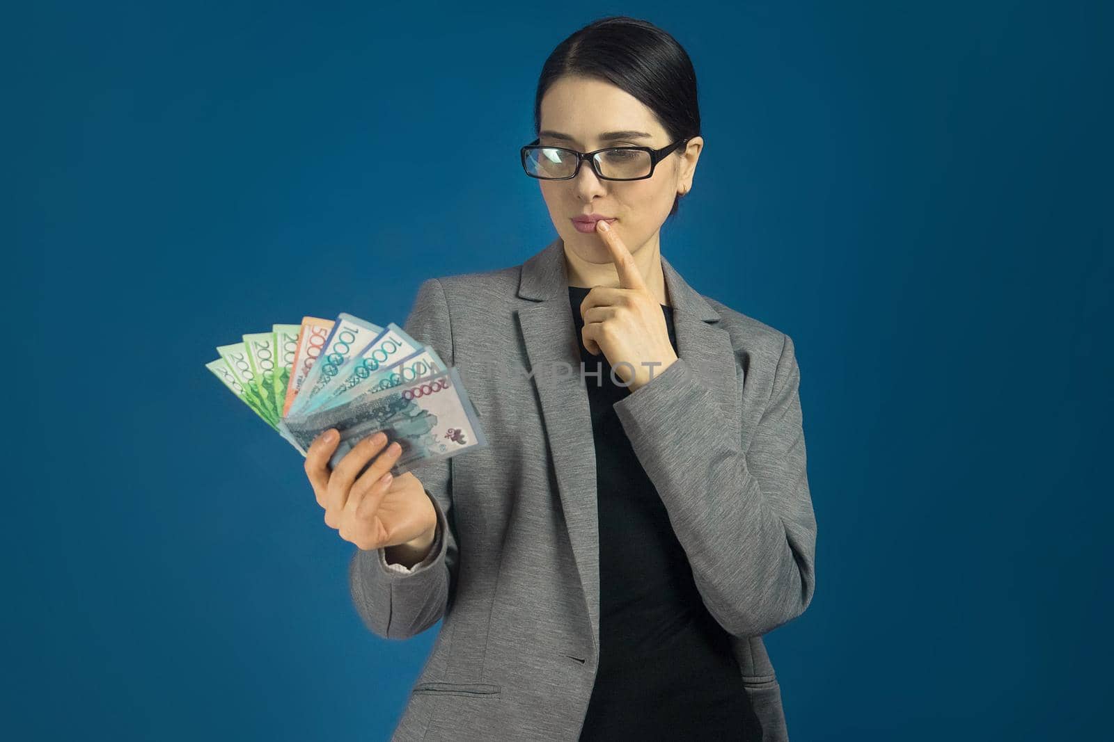 Beautiful woman in a gray jacket with a pack of tenge in her hand is thinking about shopping.