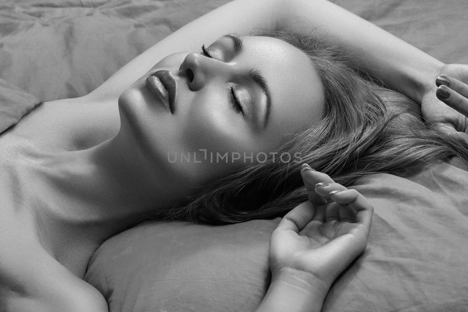 Beautiful Woman Sleeping while lying in Bed with Comfort. Sweet dreams. Sexy model with long curly hair relaxing on grey sheets. Black and white photo
