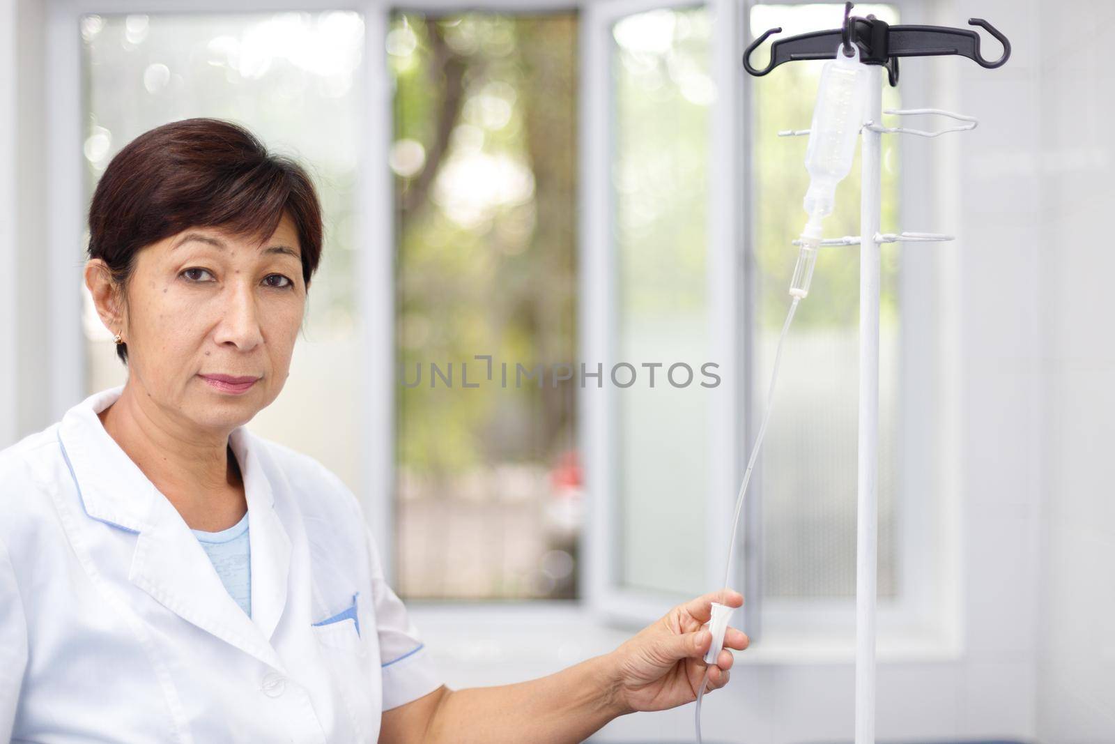 Portrait of a senior female nurse in middle asia Kazakhstan clinic intravenous drip hospital ward.