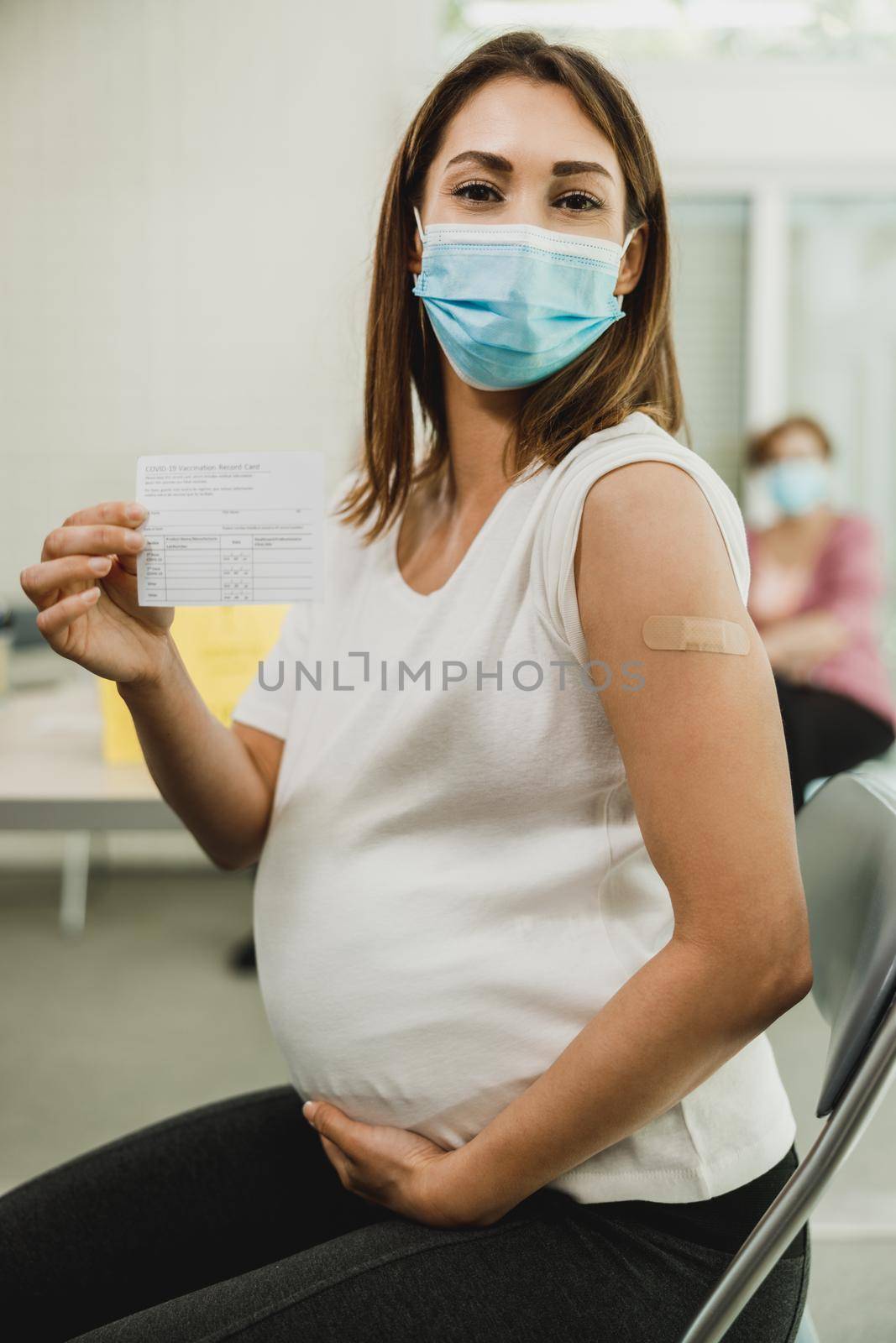 Pregnant Woman Holding Covid-19 Vaccination Record Card by MilanMarkovic78