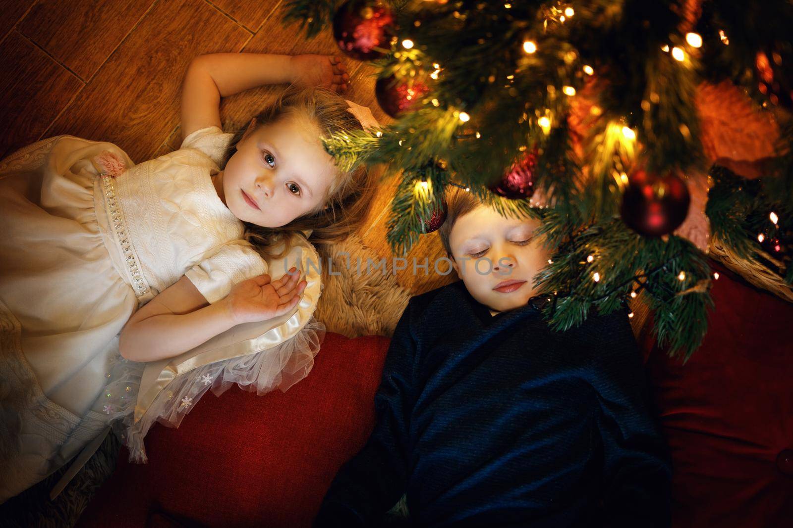 Brother and sister lies on the carpet near the christmas tree in cozy christmas interior with festive garland. Selective soft focus, film grain effect