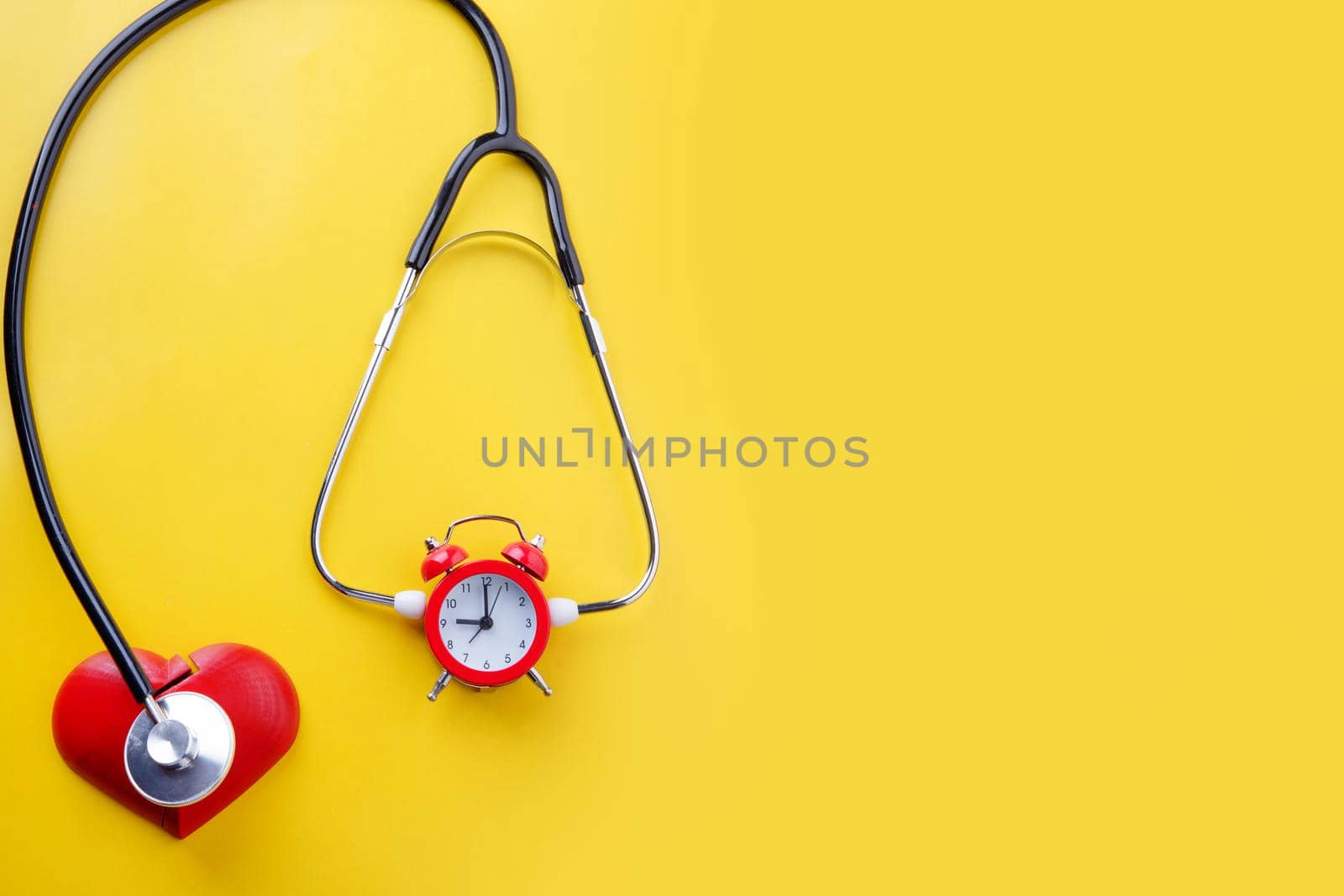 stethoscope and alarm clock on yellow background. Time to book a Health Check