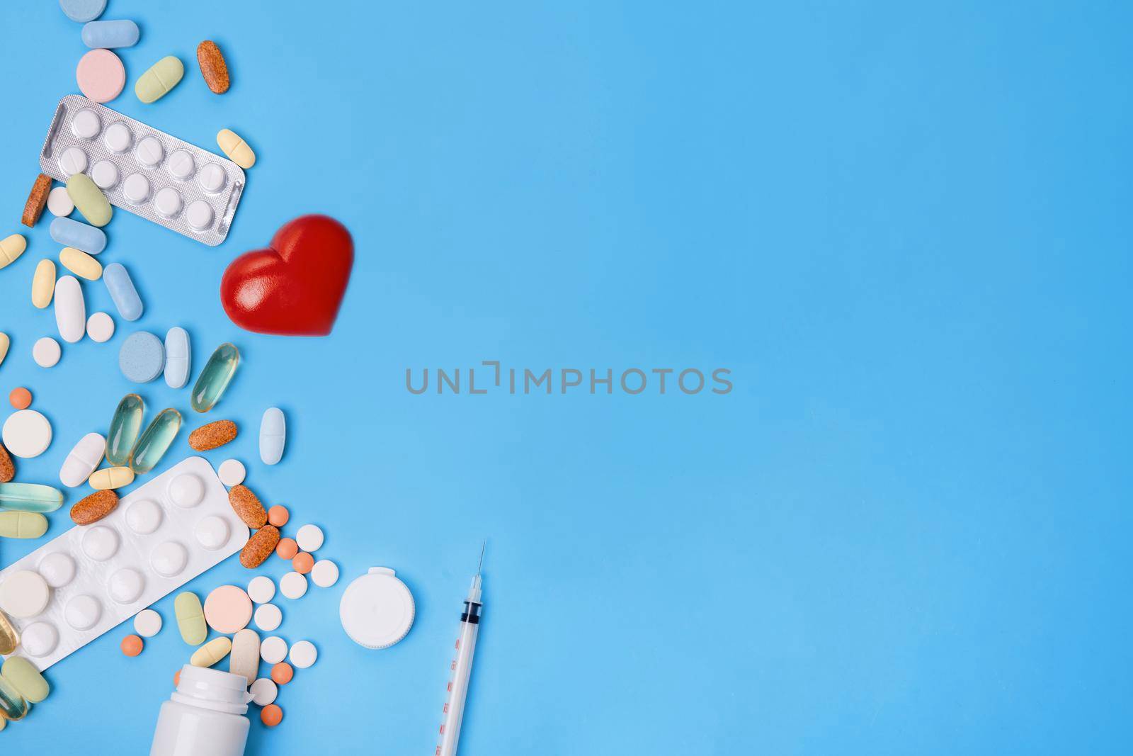 Pills, vitamins and disposable syringe, heart, stethoscope on blue background top view Space for text. see doctor.