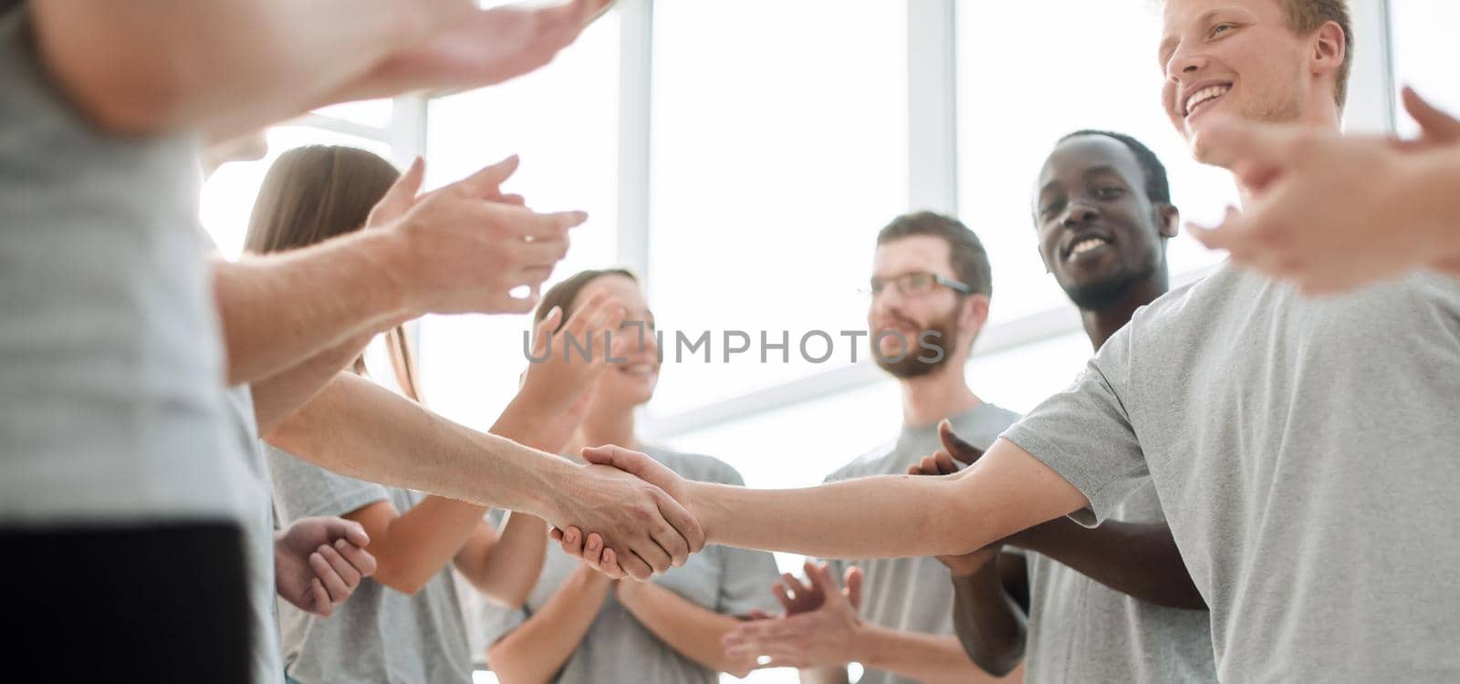 smiling young people shaking hands, standing in a circle of friends.
