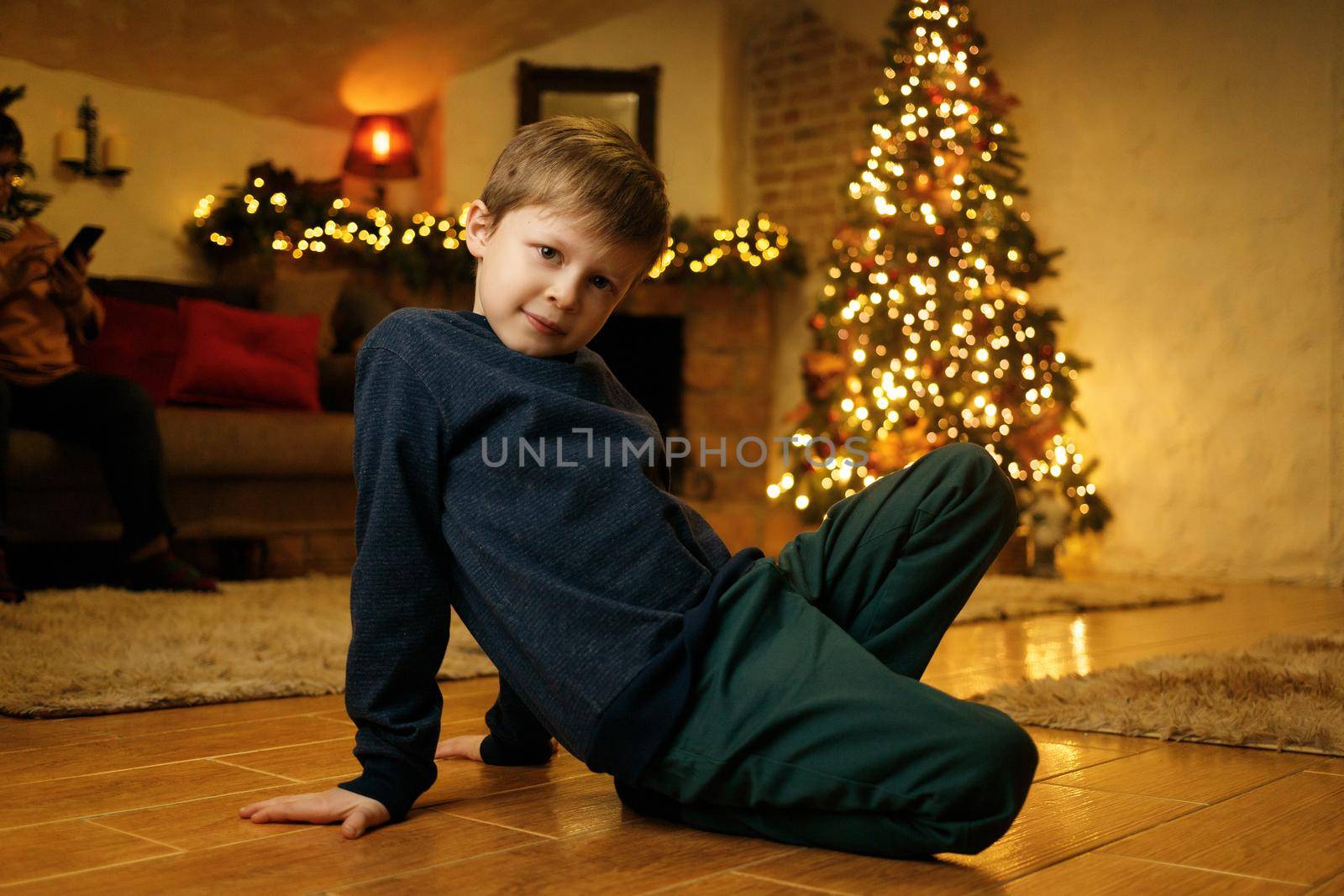 A boy sits on the floor in a festive room on the eve of the christmas holiday by Rom4ek