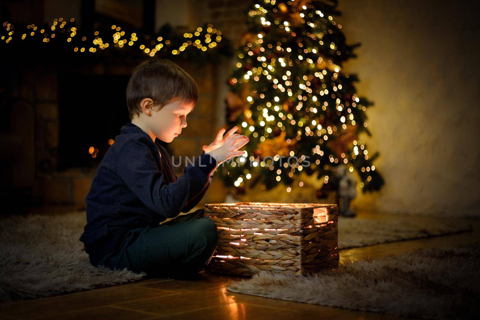 Little boy opened a magical New Year's gift in a Christmas interior with a Christmas tree and garlands. Selective soft focus, film grain effect