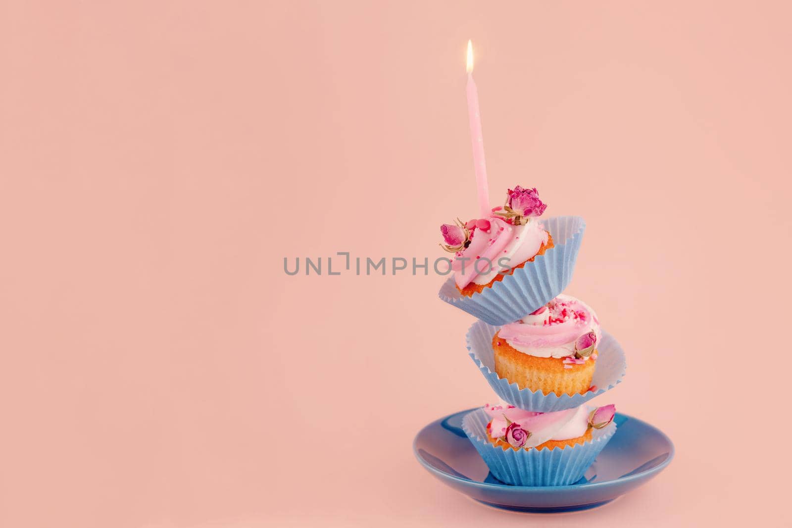 three birthday berry muffins on top of each other in blue wrappers with a candle on top on a saucer on a pink background. high-quality photos for calendar and cards. Space for text