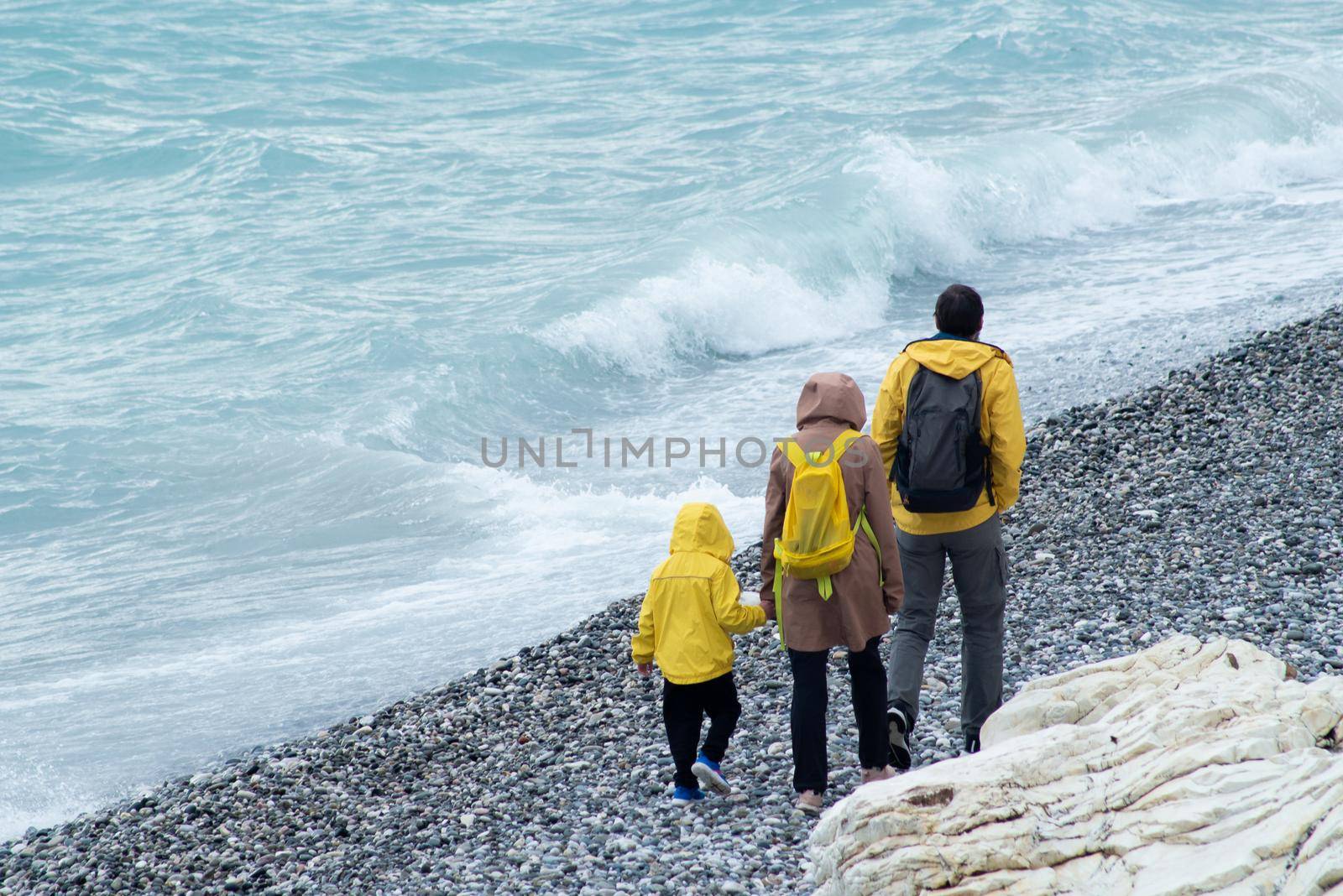 SOCHI, RUSSIA - MAY 09, 2022: a man, a woman and a child walk along a pebble beach in yellow raincoats