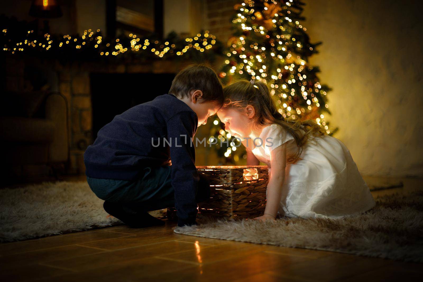 Boy and girl opened a miracle New Year's gift in a Christmas interior with a Christmas tree and garlands. Selective soft focus, film grain effect