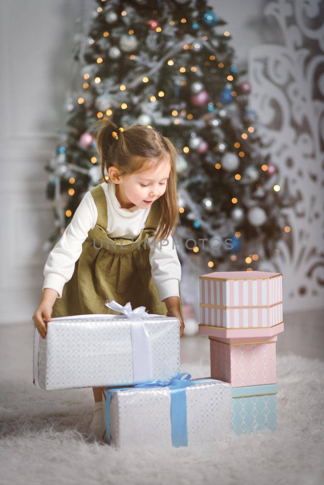 Little girl playing with new year gifts in living room with christmas tree.