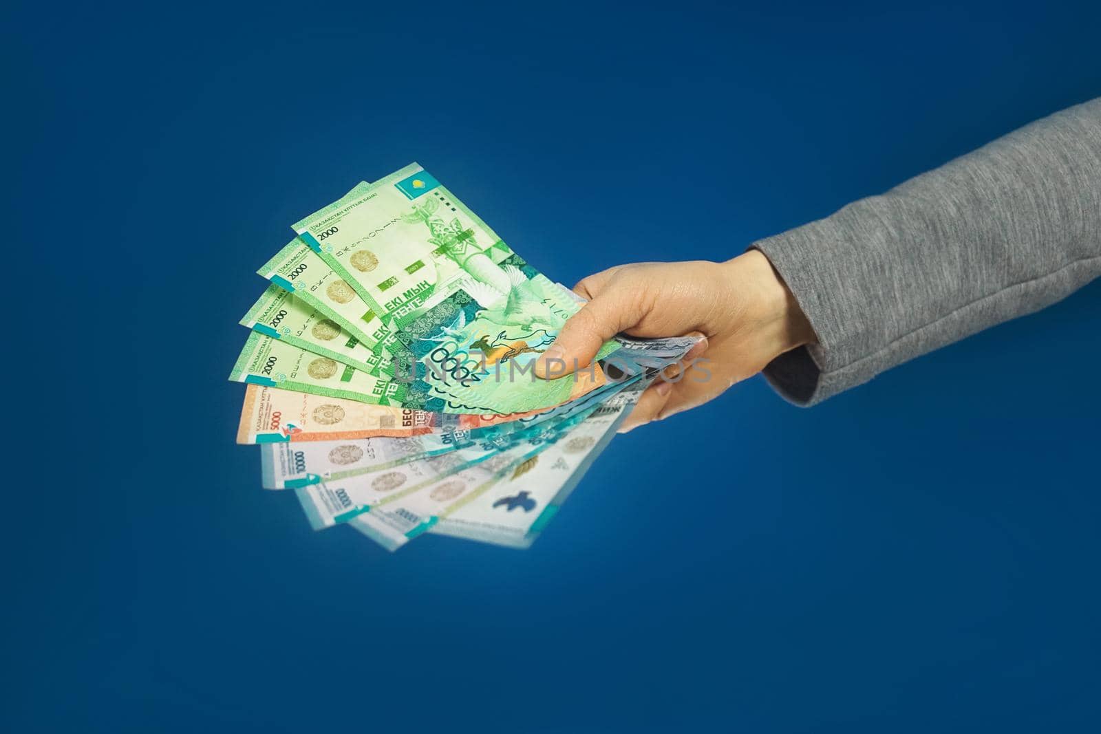 Tenge National money of Kazakhstan in hand on blue background. Selective focus.