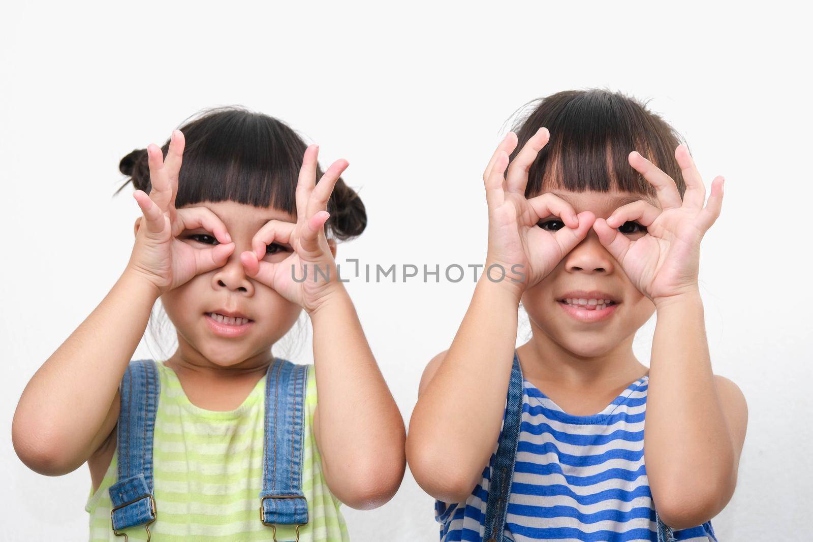 Two little sisters make glasses from fingers and smiles looking at the camera isolated on white background. friendship and love concept.