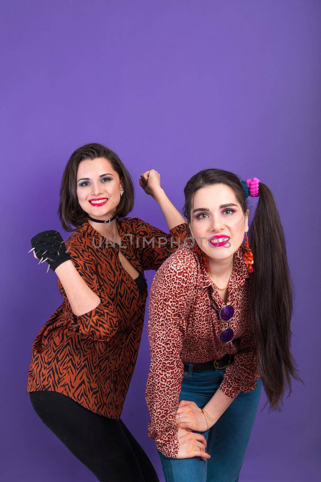 Party in retro 90s and 80s style. Two young women on violet background with copy space.