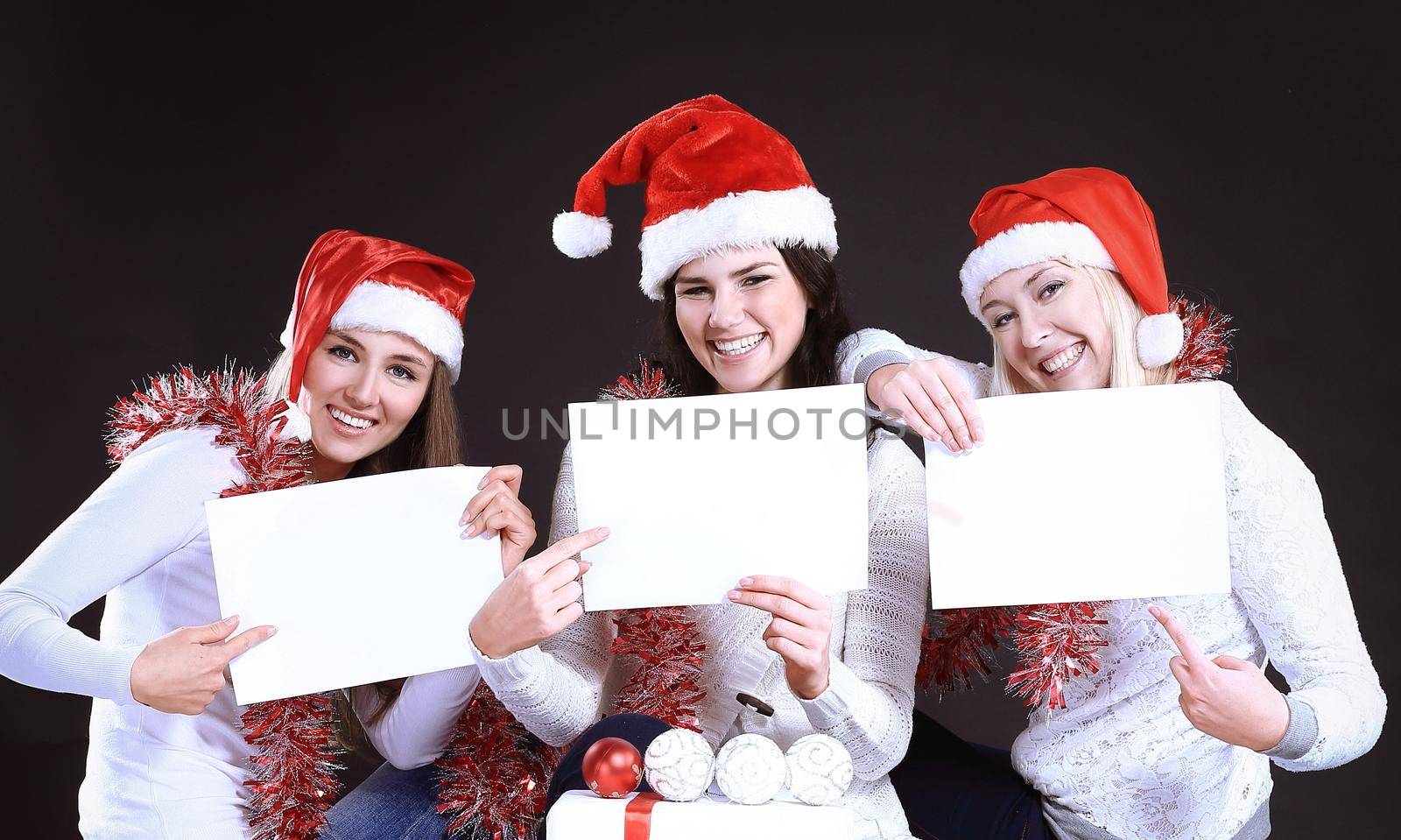 three young girls in costume of Santa Claus showing blank sheets. isolated on black