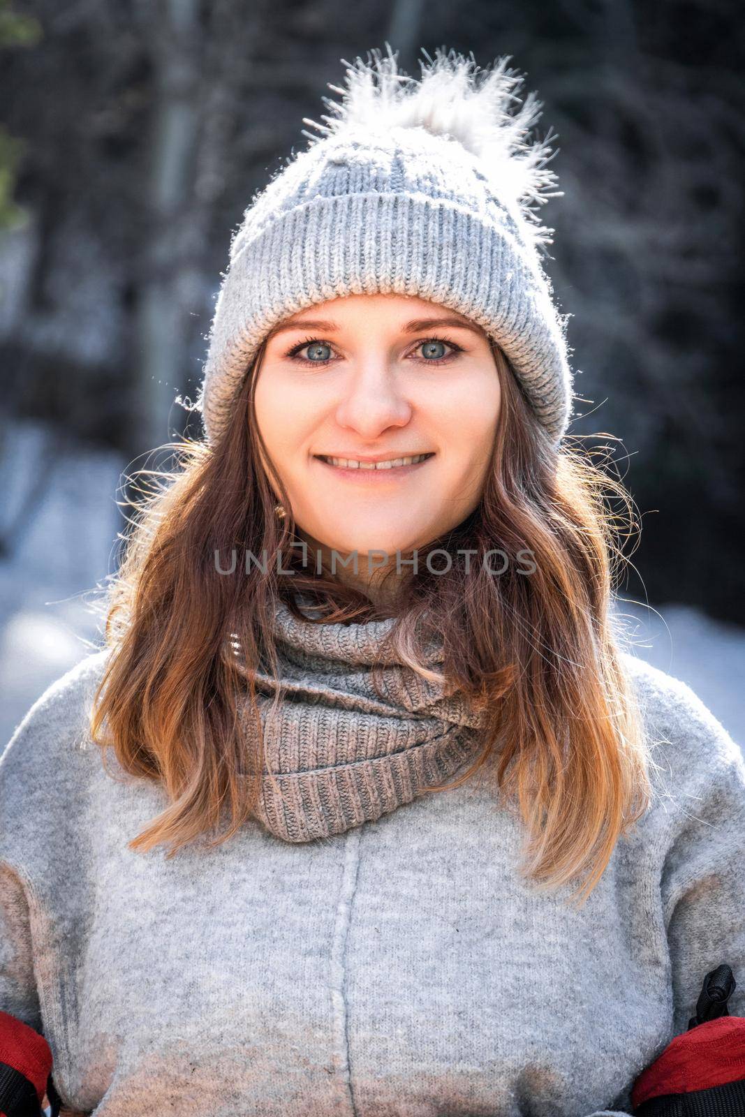 Winter vertical portrait of caucasian blond young smiling happy woman in grey sweater and beanie hat outdoor.