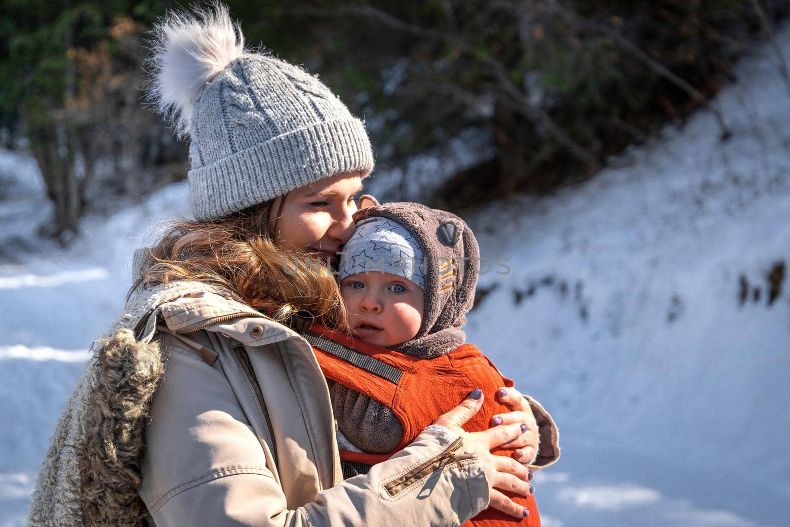 Side view of young caucasian babywearing mother with his baby in baby carrier walking outdoor.