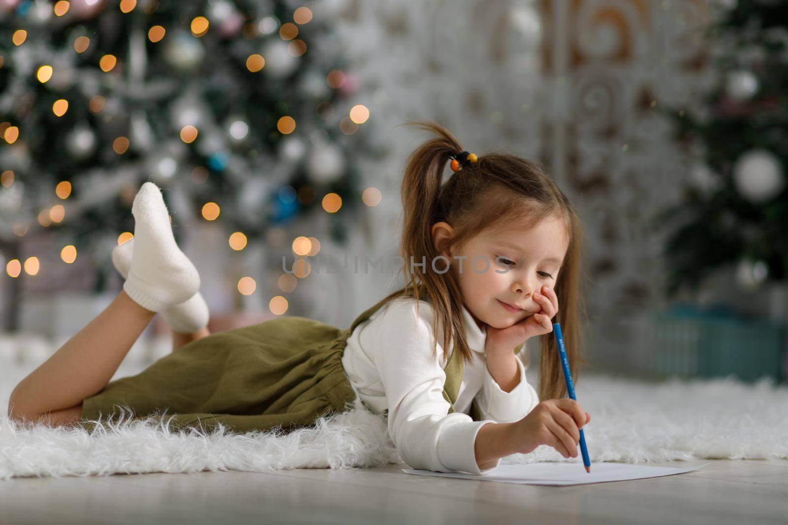 Cute little girl with ponytails is writing a letter to santa claus in christmas interior.
