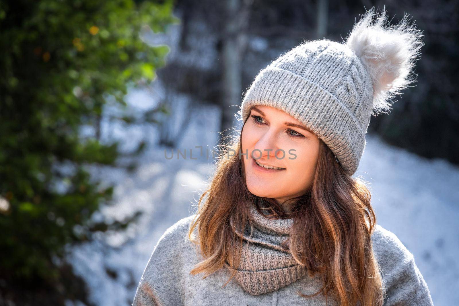 Winter portrait of blond young woman in grey sweater and beanie hat outdoor.