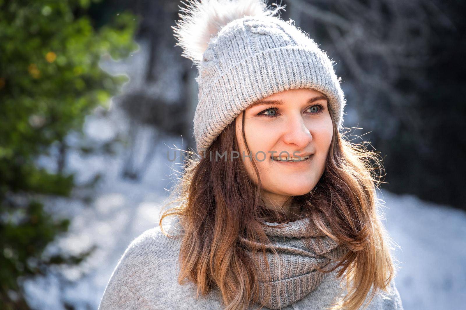 Winter portrait of caucasian blond young smiling happy woman in grey sweater and pompom hat outdoor.