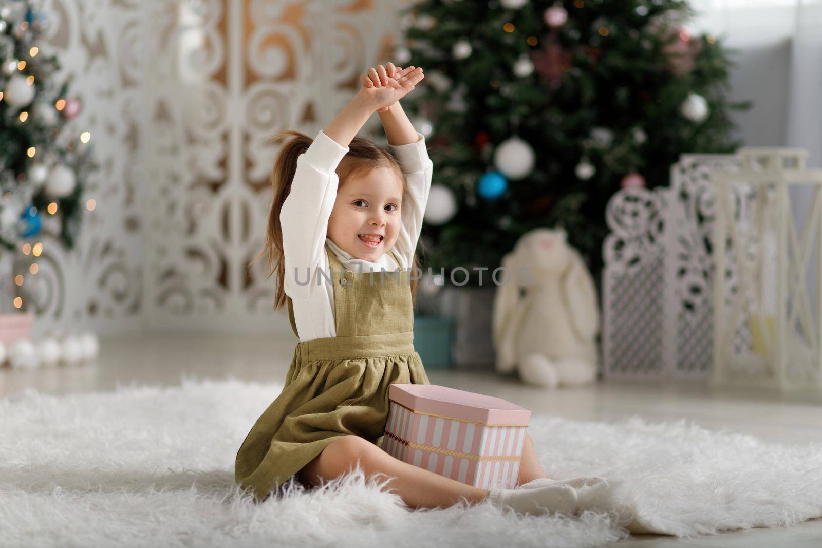 Little happy girl with new year gift while sitting on the carpet in christmas interior.