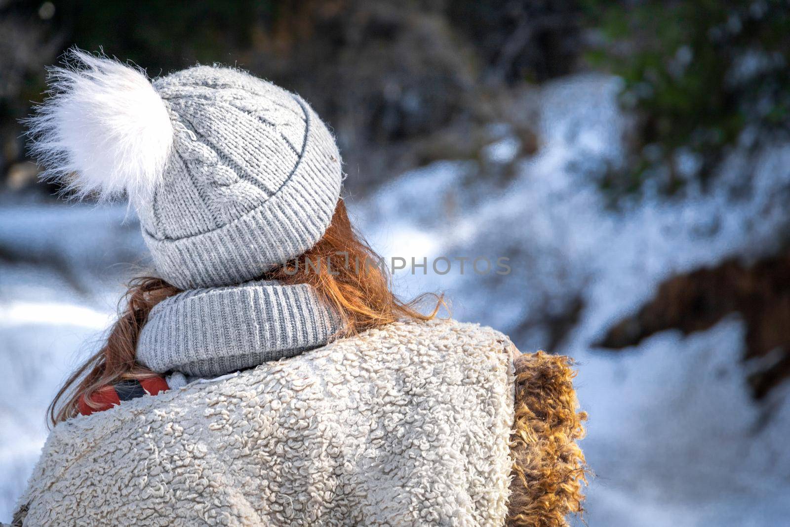 Rear view on blond young woman in winter clothes and beanie hat outdoor.