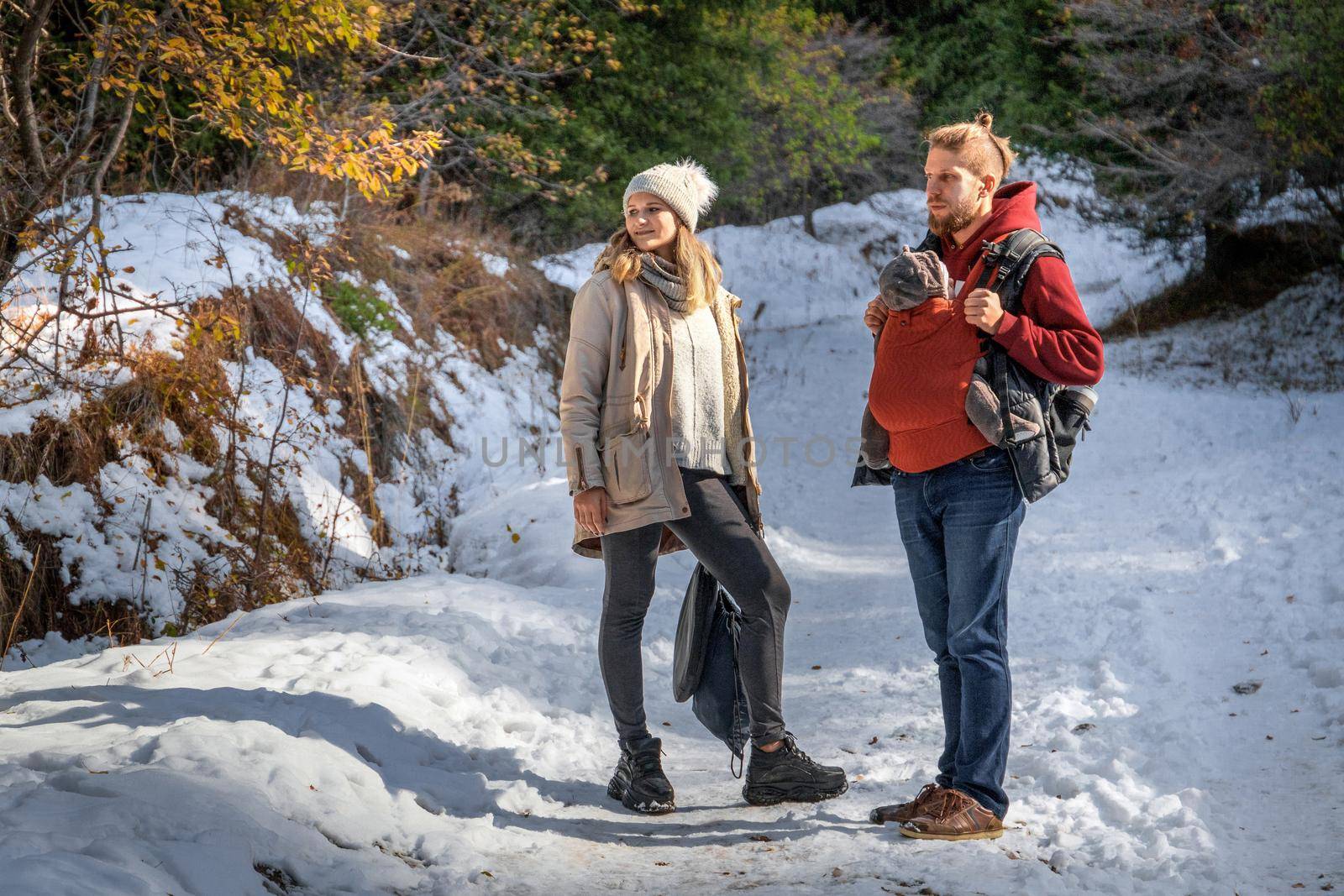 Young family with their baby boy in ergonomic baby carrier in winter nature.