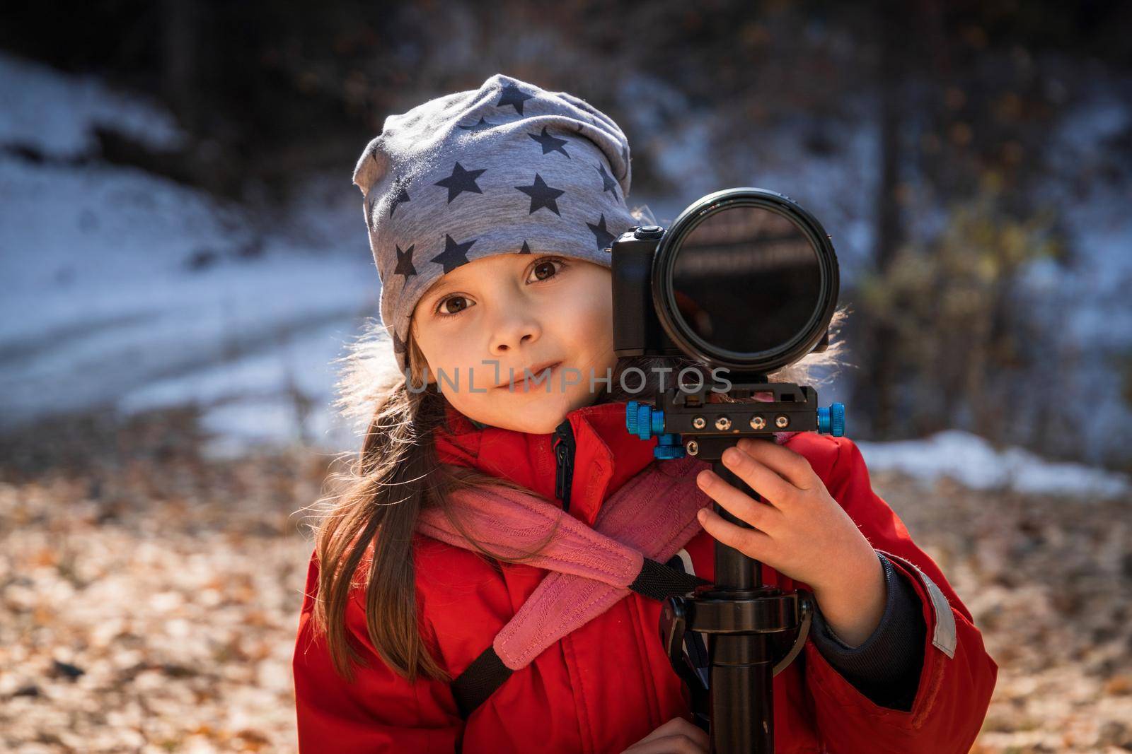Portrait of happy little girl with camera in star hat outdoors.