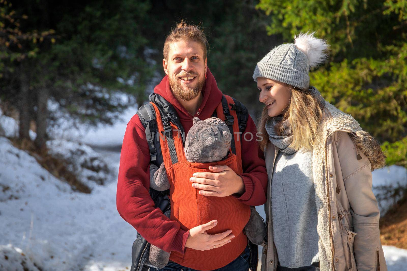 Babywearing winter forest walk with family and their baby son in ergonomic carrier.