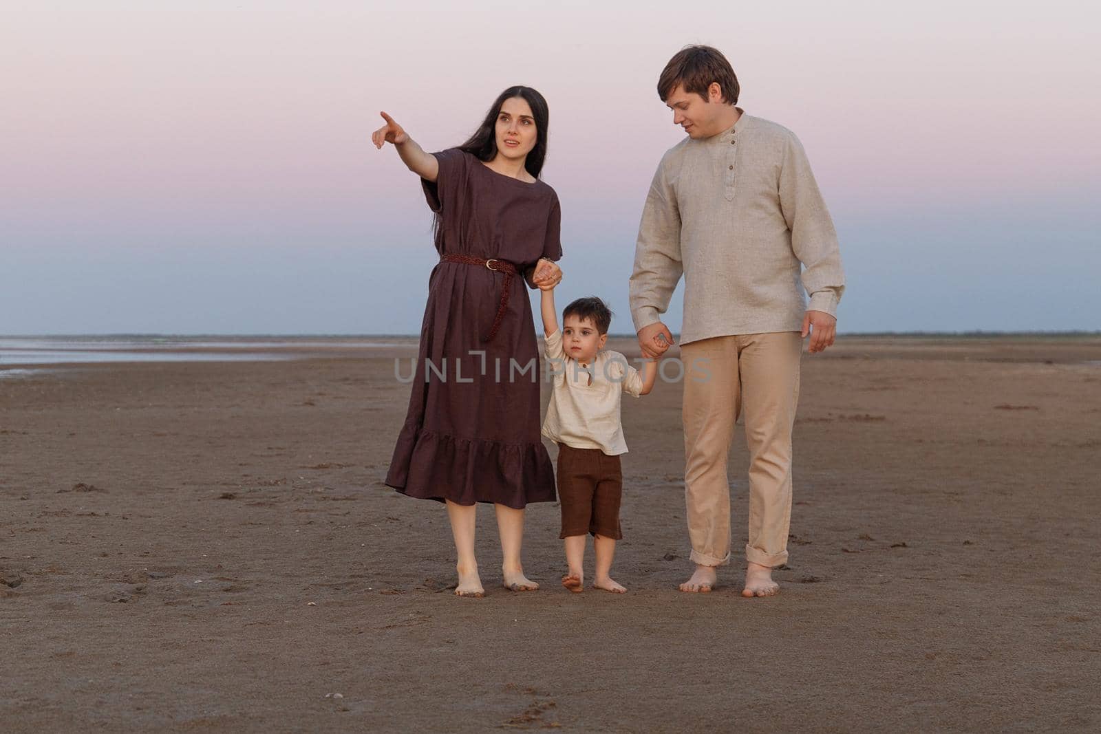 Beautiful young family spend time together walking along the deserted evening shore.