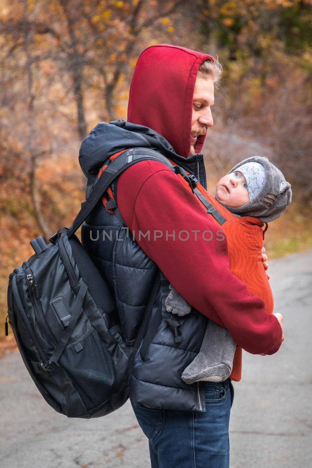 Young father with his baby in ergonomic baby carrier in autumn hiking. Babywearing and active father concept.