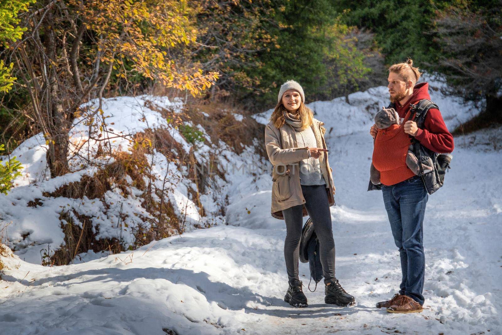 Young family with their baby boy in ergonomic baby carrier in winter forest hiking.