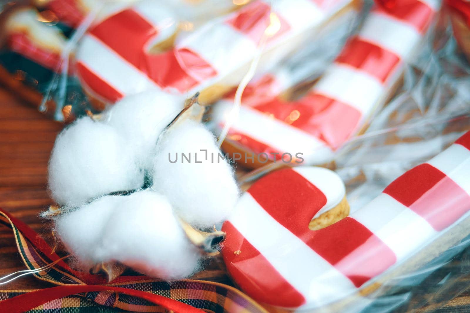 Close up of Christmas sweets in bags with ribbons. Gingerbread in form of sugar canes on wooden table. Cookies with red and white icing in stripes.