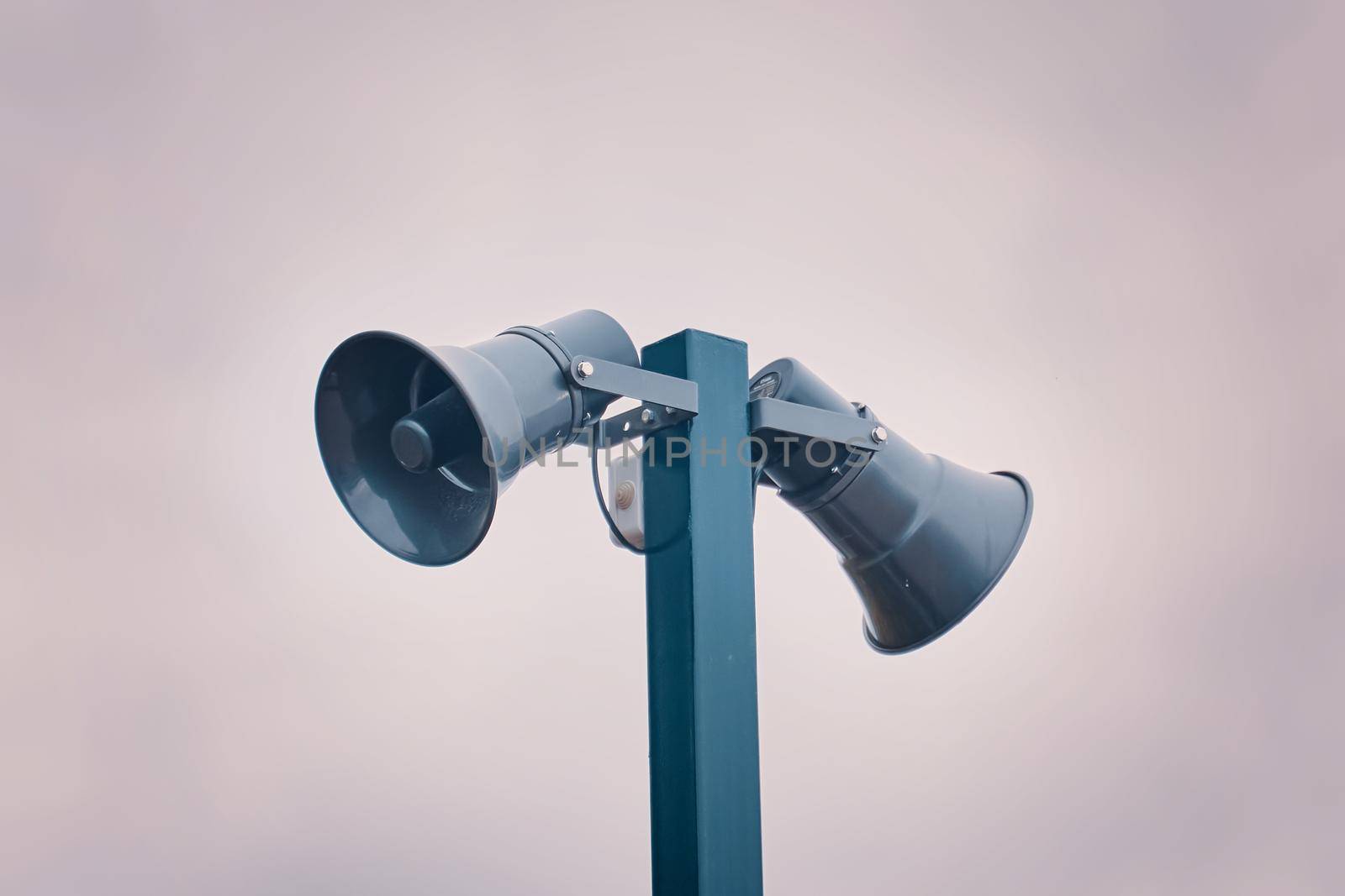 Hazard warning system. Tall metal column with two gray loudspeakers against cloudy sky. Providing security in the city, notification of emergencies. Copy space for text.