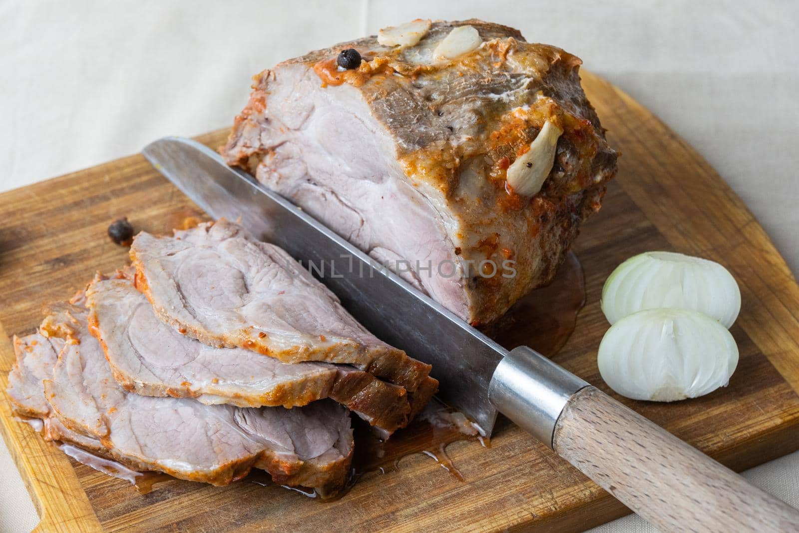 juicy meat pork neck in a marinade with garlic and pepper baked in the oven lies on the cutting board. Several steak-like slices are cut from it. Next to it is half an onion by olex