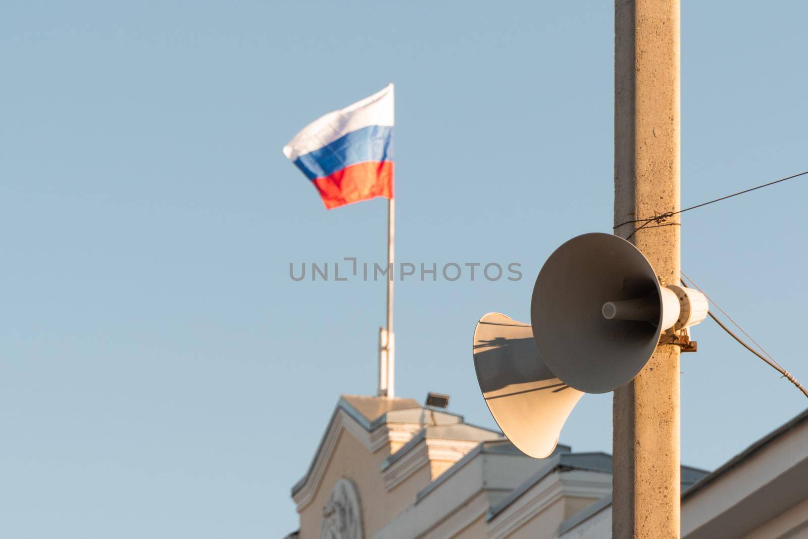 loudspeakers on the electrification pole. in the background, the Russian flag is flying on the administrative building by olex