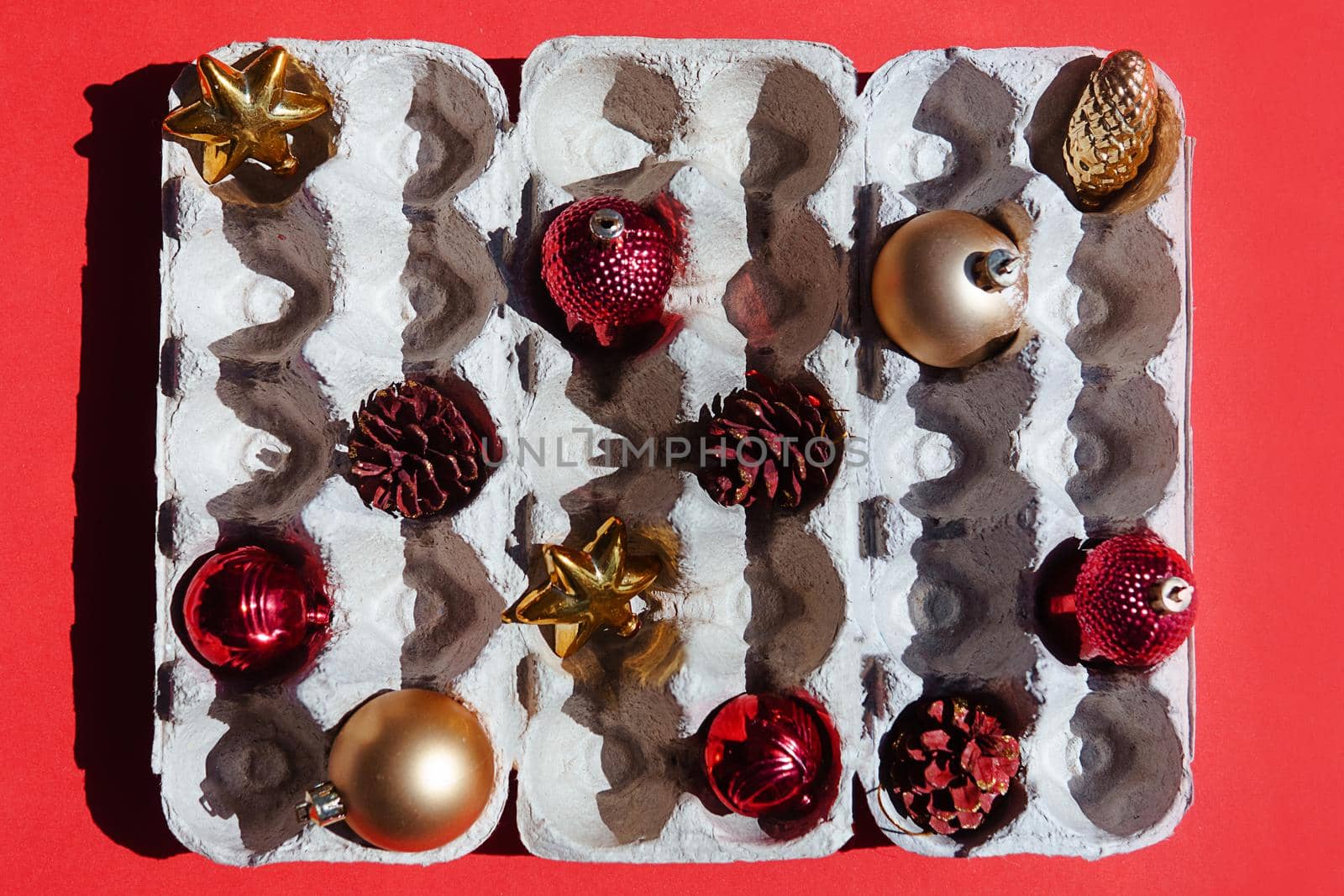 Christmas tree toys in the egg tray on a red background. Top view. The concept of New Year's holidays and Christmas. Red and gold colors.