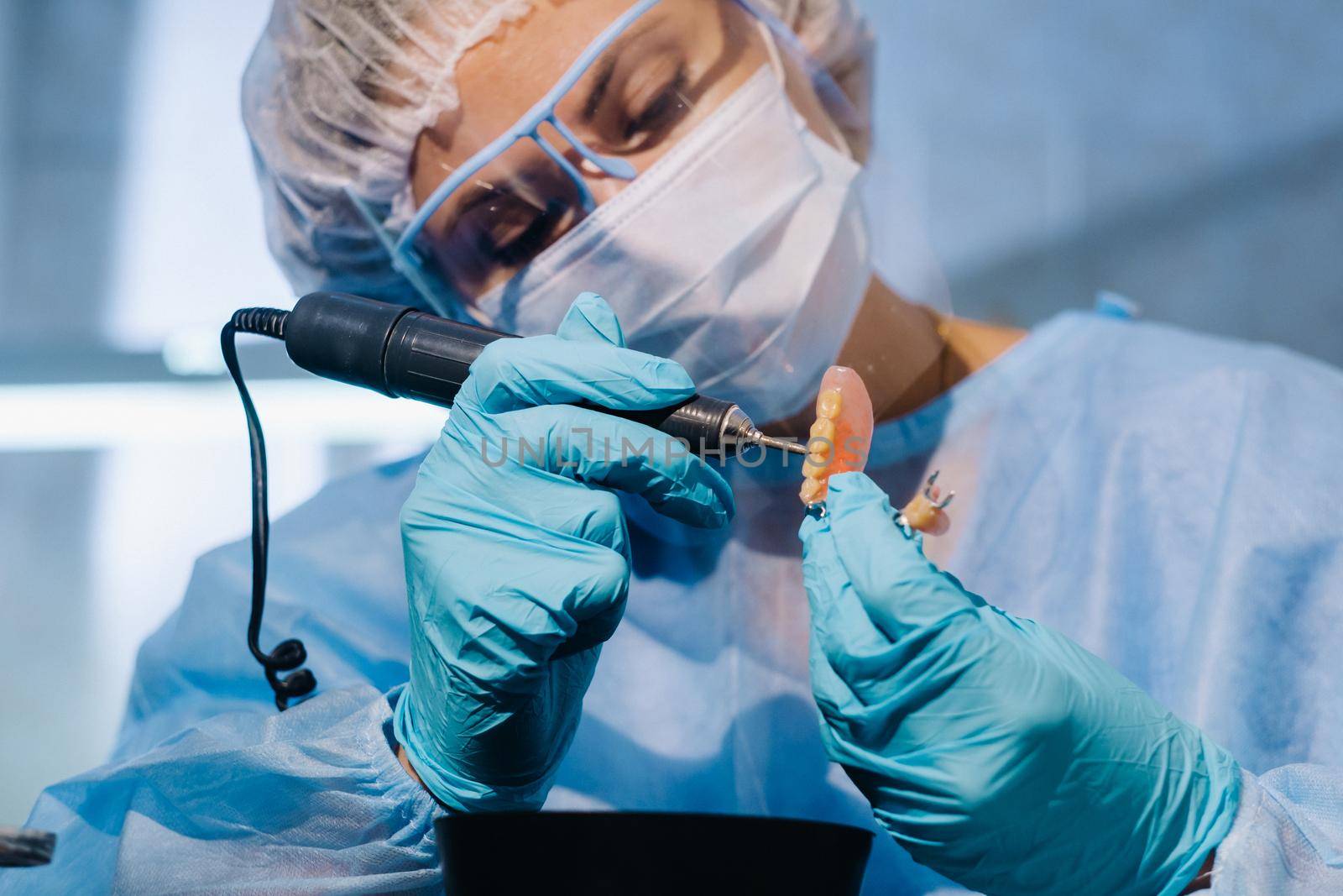 A dental technician in protective clothing is working on a prosthetic tooth in his laboratory.