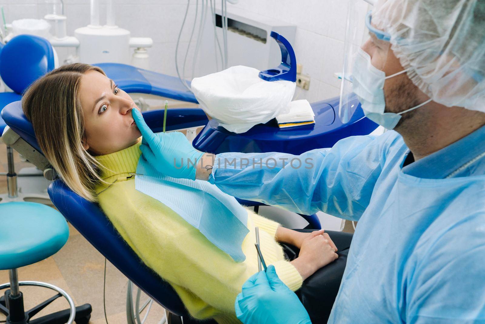 a dentist wearing a protective mask sits down next to the patient and covers his mouth with a finger by Lobachad