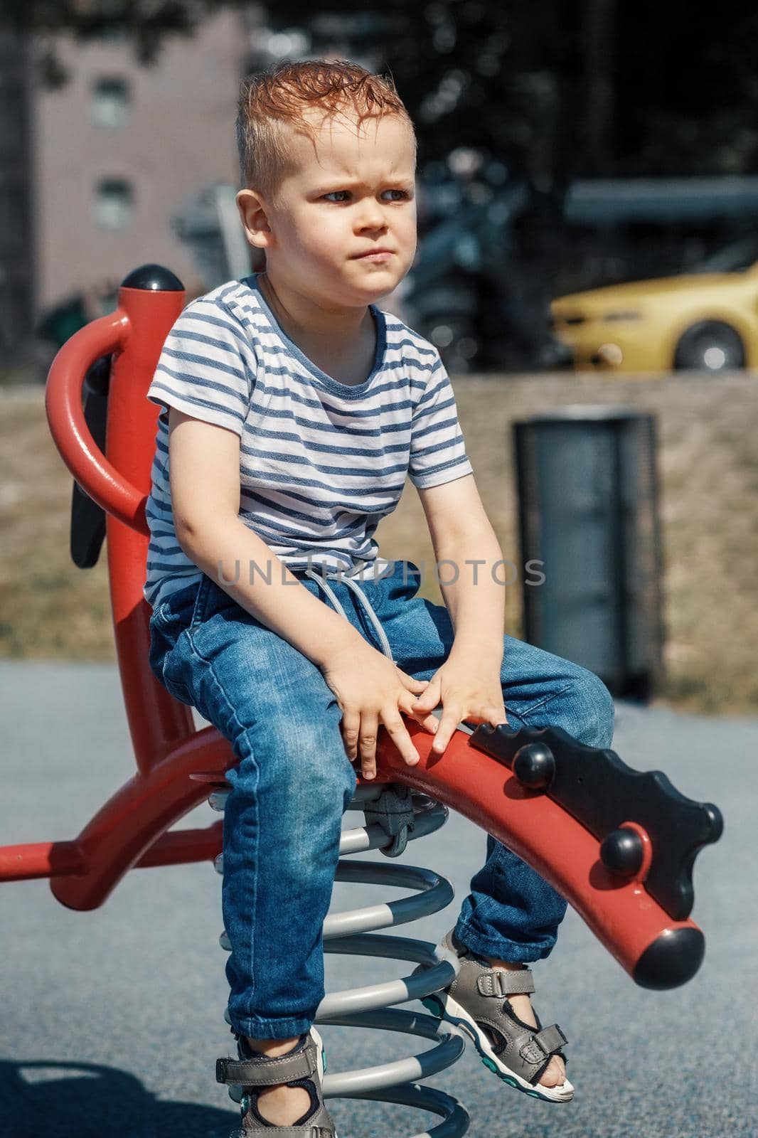 A thoughtful boy on a spring swing in a playground.