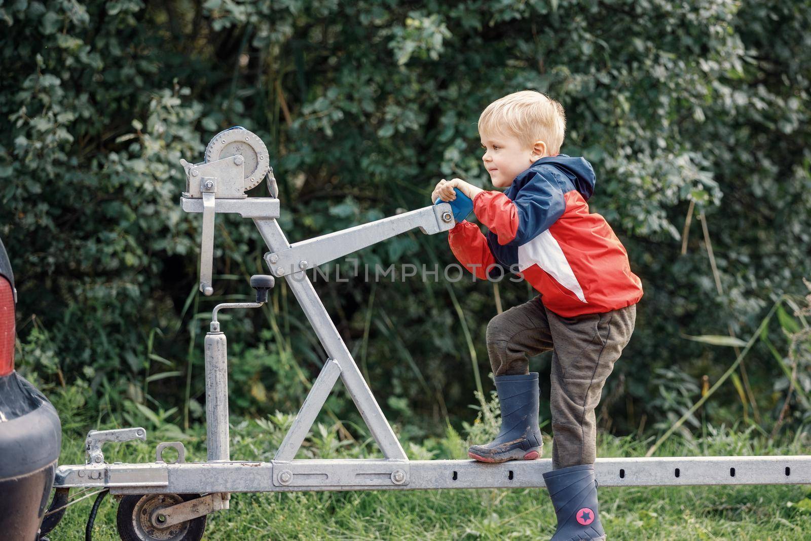 An agile child sports on a boat trailer mechanism in nature by Lincikas