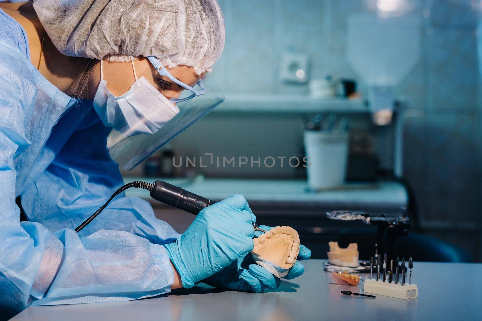 A dental technician in protective clothing is working on a prosthetic tooth in his laboratory.