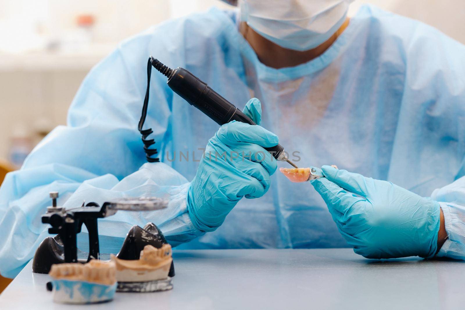 A masked and gloved dental technician works on a prosthetic tooth in his lab.