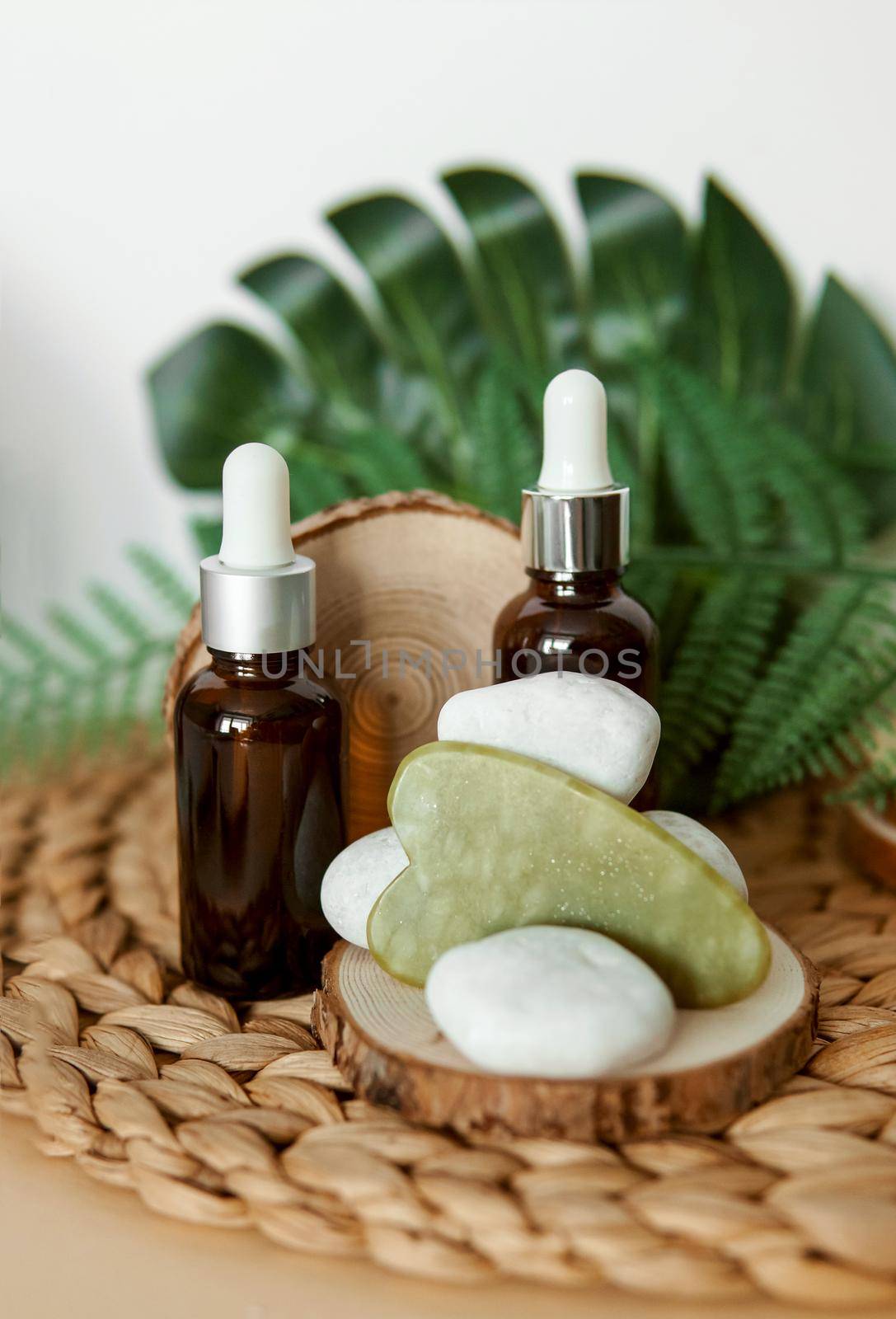 Jade Gua sha scraper and bottles of cosmetic serum for the face on wooden stands. Concept zero waste.